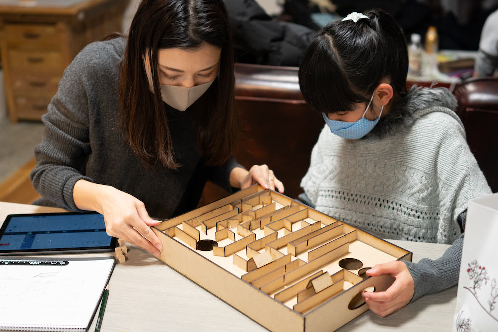 Kid and mentor making a marble labyrinth game